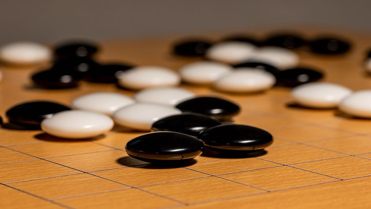 Black and white Go stones in play on a wooden board, raking light.